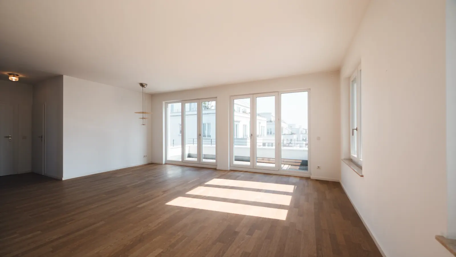 Leere, helle Wohnung mit Parkett, Sonnenlicht fällt durch hohe Fenstertüren